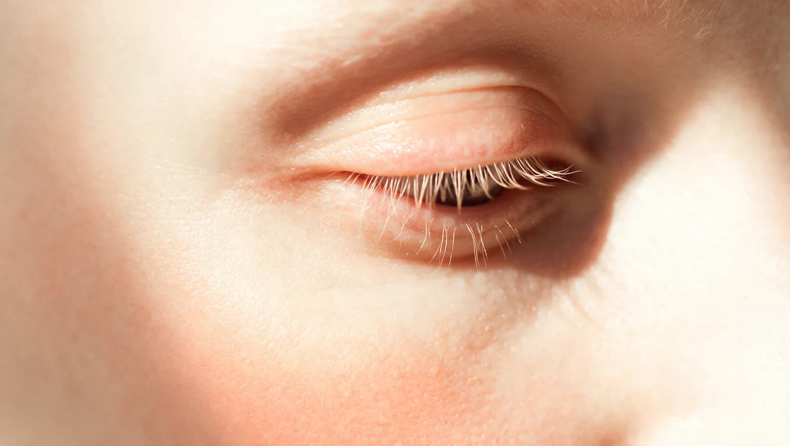 Macro du contour de l’œil d’une femme à la peau claire, sans maquillage, lumière latérale révélant le relief de la zone