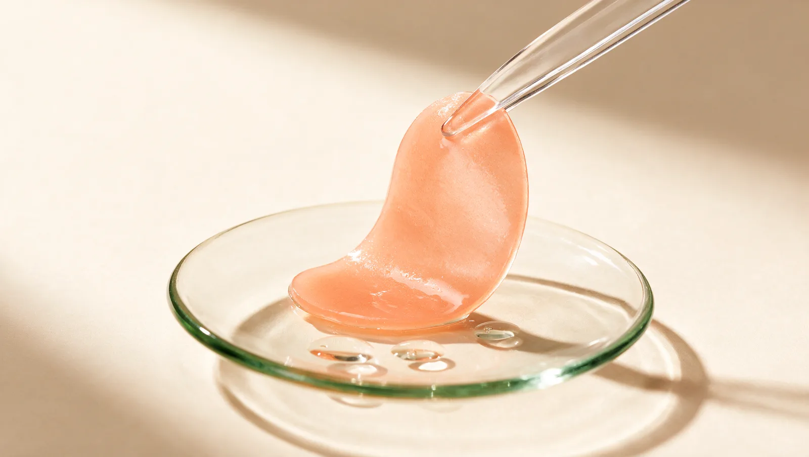 Spatule transparente soulevant un patch hydrogel pêche au-dessus d’une soucoupe en verre